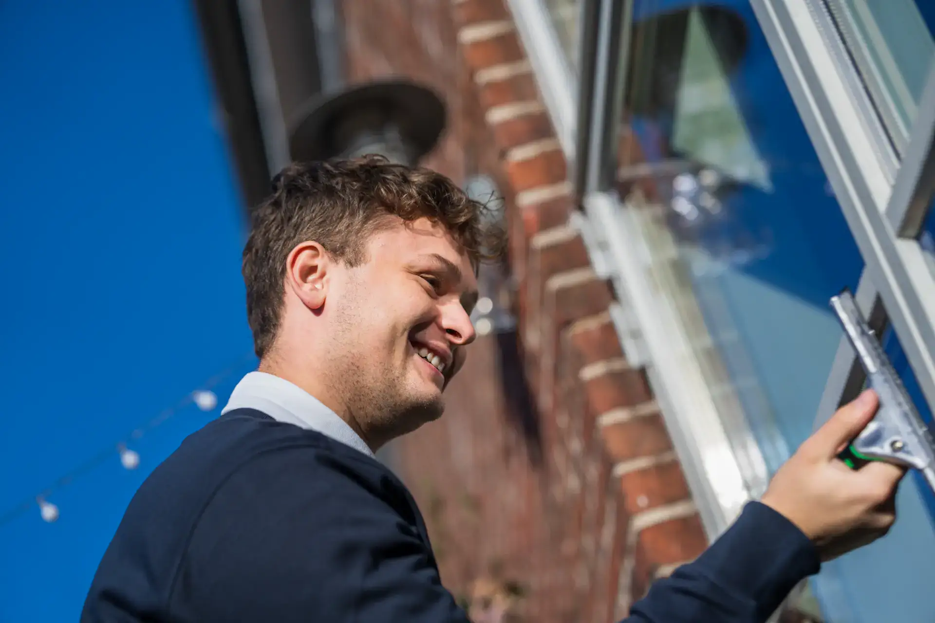 Mand rengør udendørs vindue med skumskrubber, professionel vinduespolering.