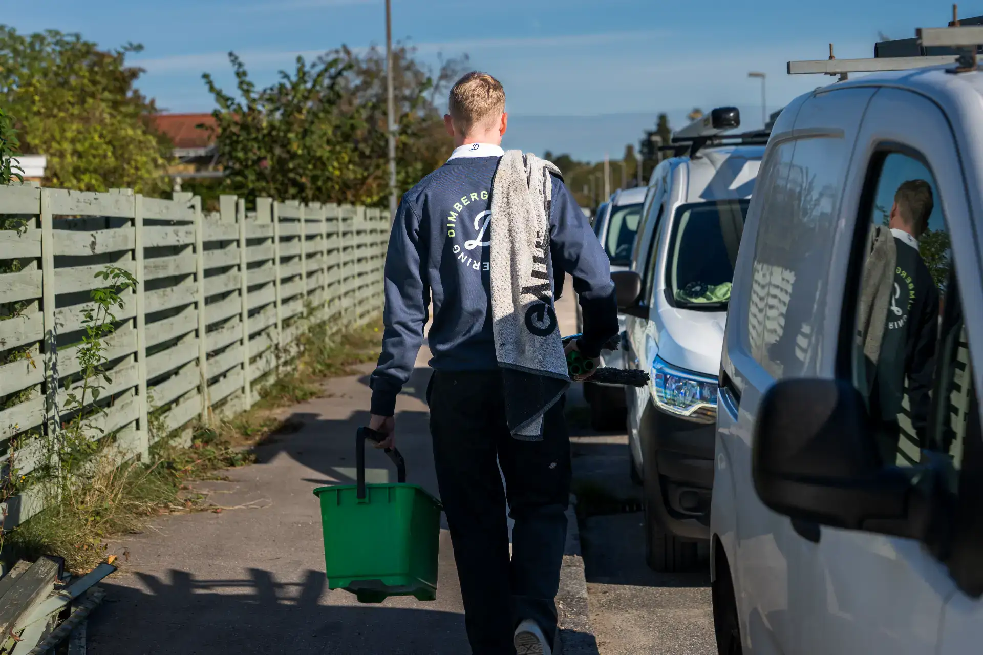 Vinduespudser går mod bil med rengøringsudstyr.