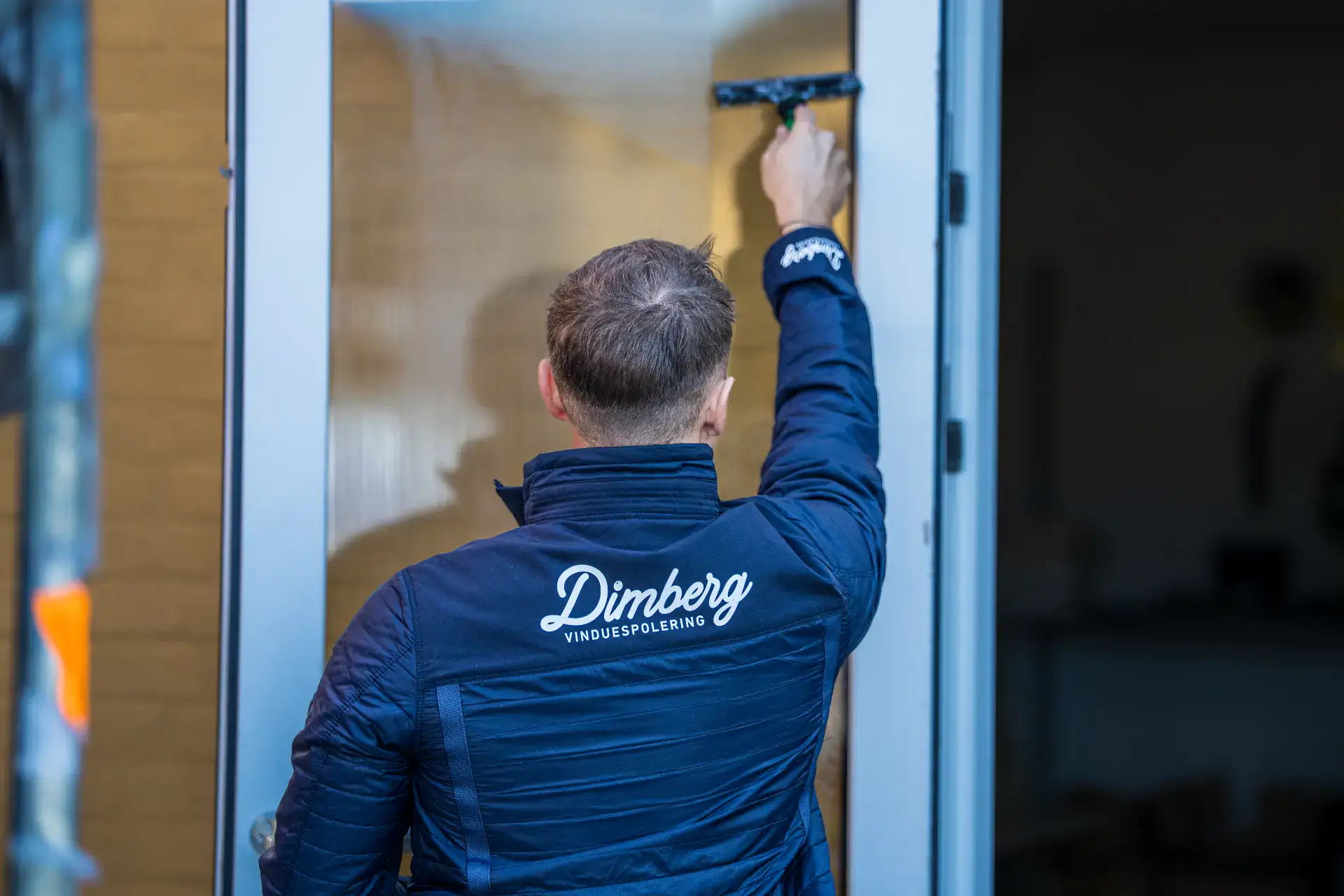 Vinduespudser rengør glasdør med skuresvamp hos Dimberg ApS.