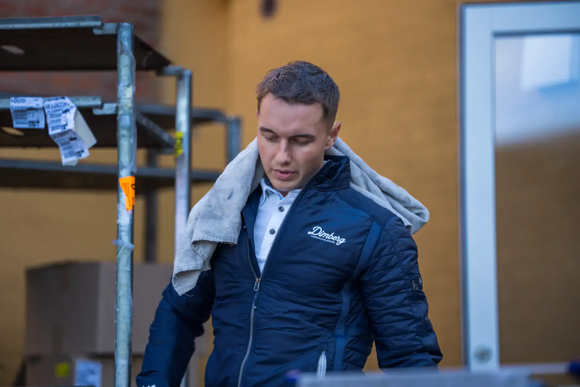 Mand, der udfører vinduespudsning indendørs, iført arbejdstøj med logo.